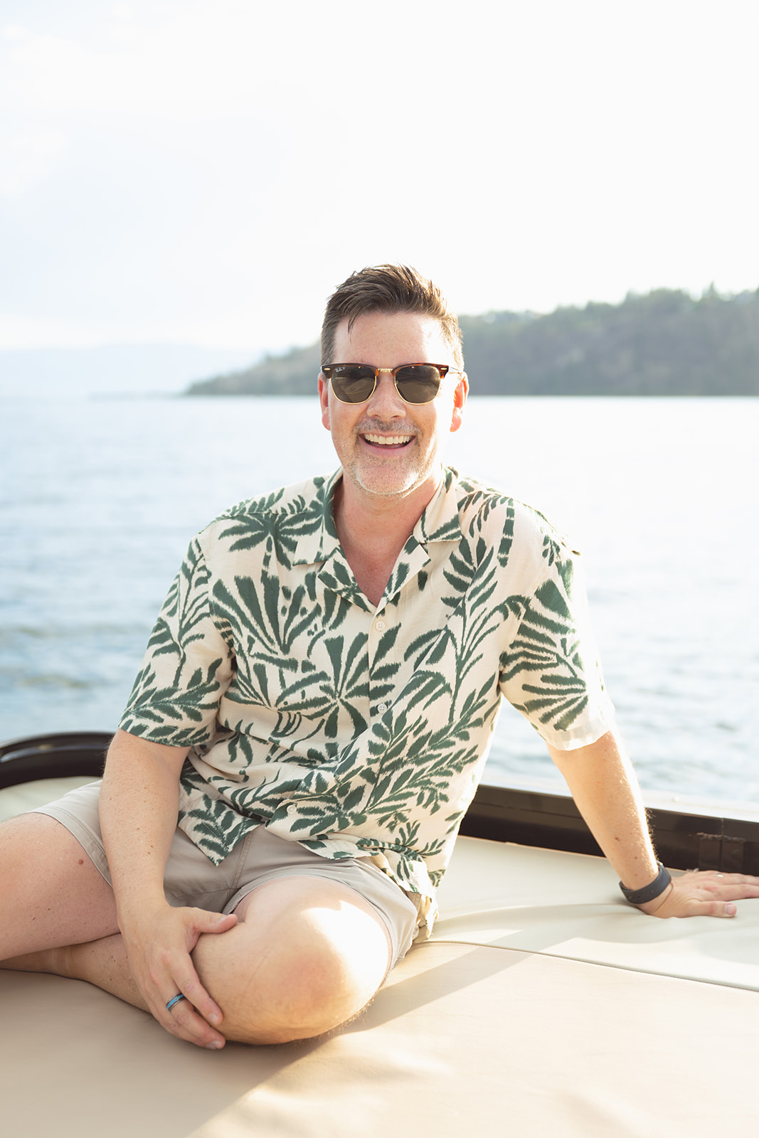 A guest in a leaf-print shirt smiles on the rooftop sun bed.
