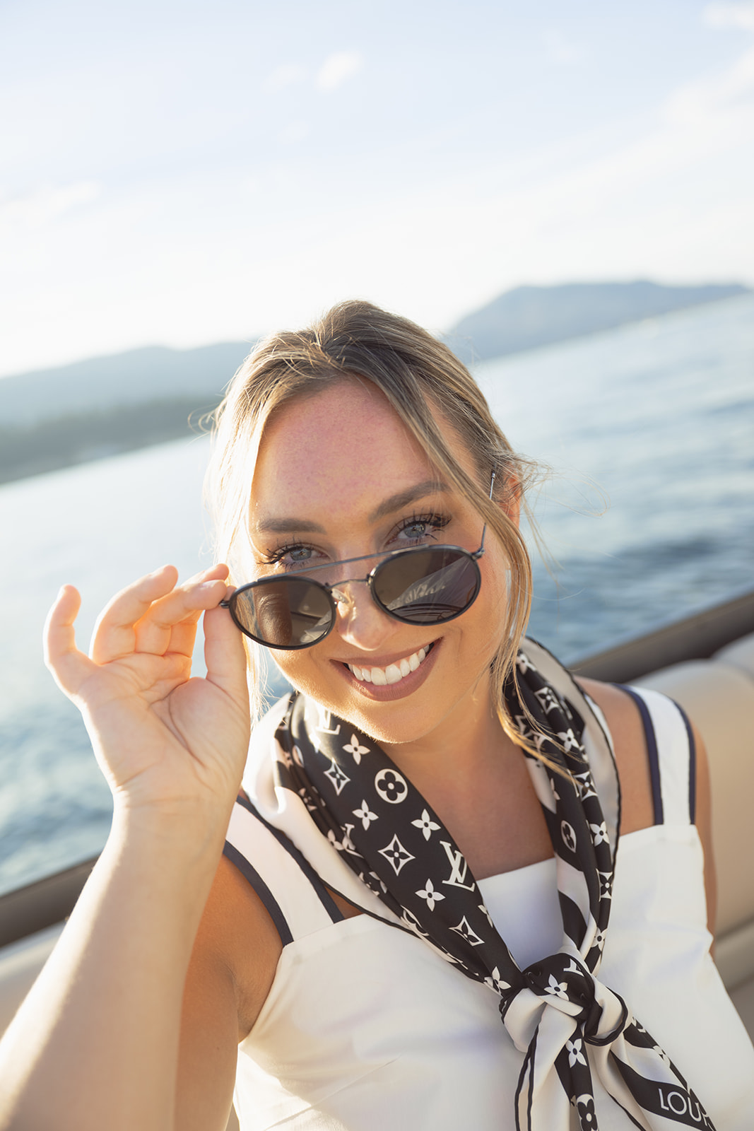 A smiling guest lowers her sunglasses with the lake behind her.