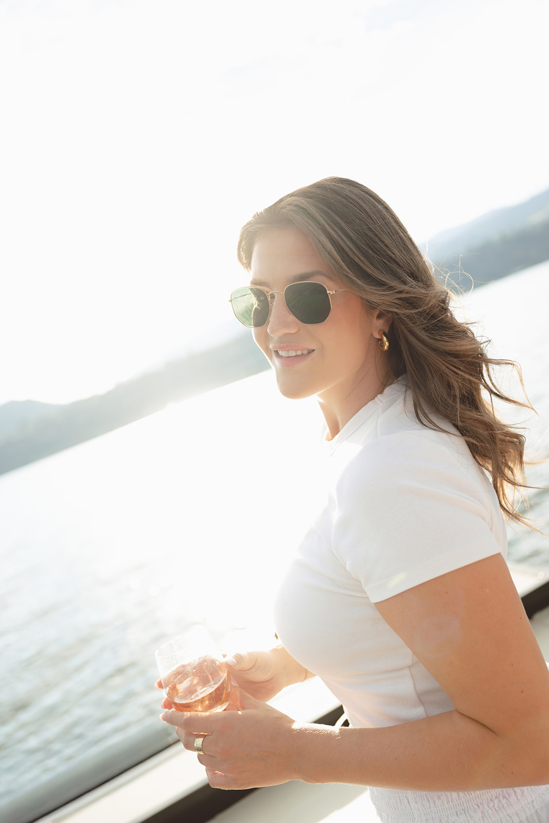 A smiling guest holds a glass beside the lake.
