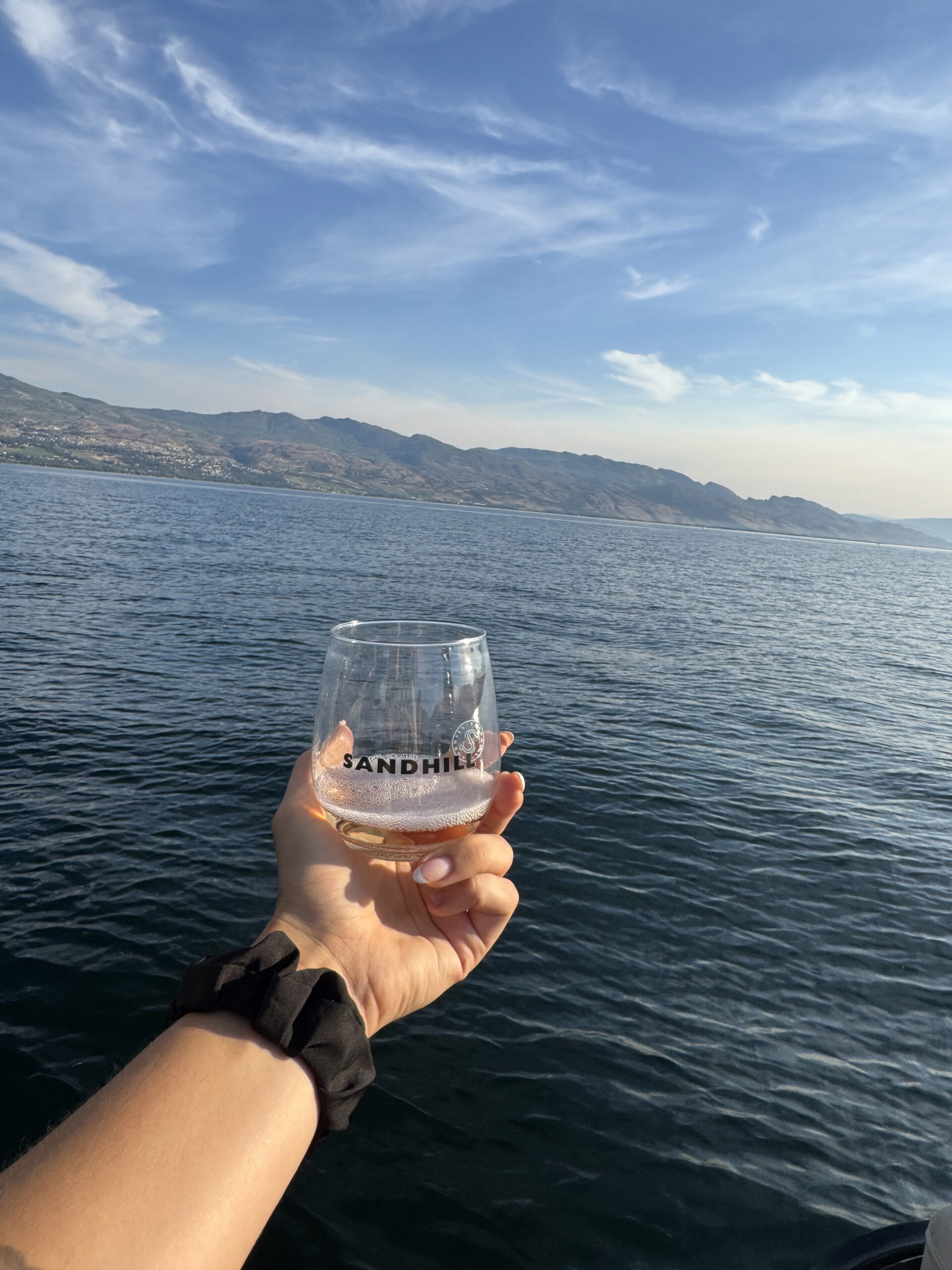 Hand holds a branded Sandhill tasting glass above the blue lake.