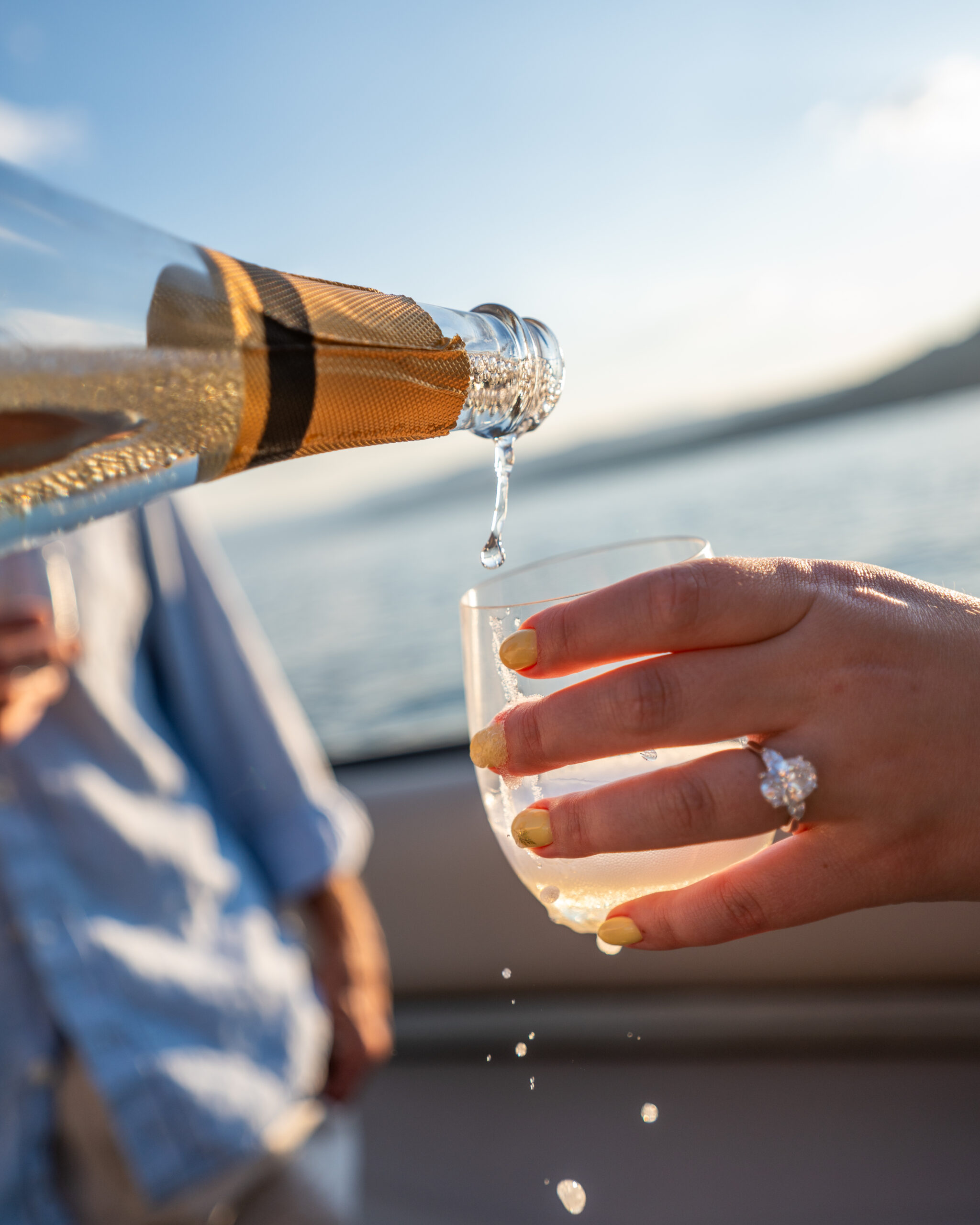 Sunlit sparkling-wine pour into a guest-held glass against the lake.